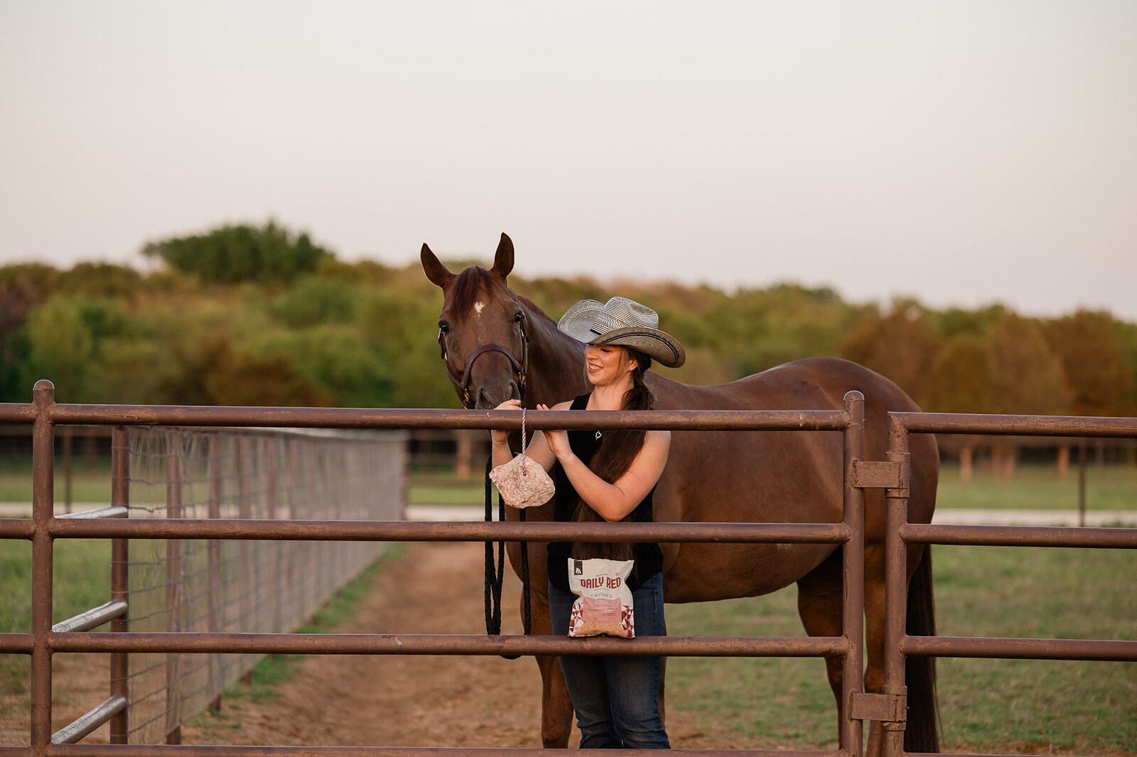 A woman standing with her horse ties Redmond Rock on a Rope salt lick on a fence.