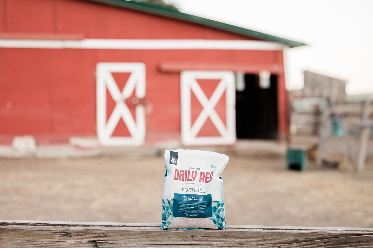 A bag of Daily Red Fortified horse minerals on a fence in front of a red barn.